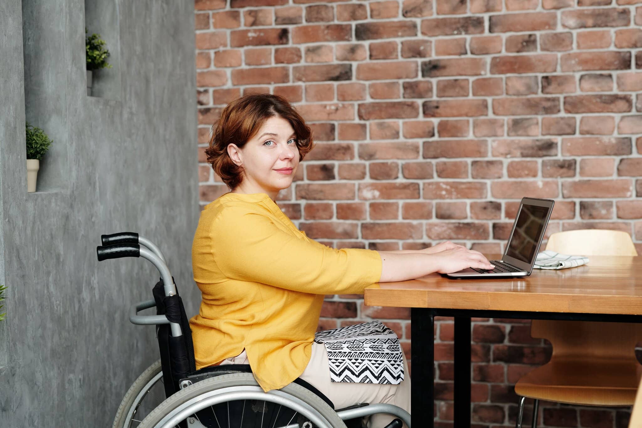Lady with a red jacket, she is in a wheelchair looking forwards with a warm smile. She has her laptop, she is about to start a disability counselling session.
