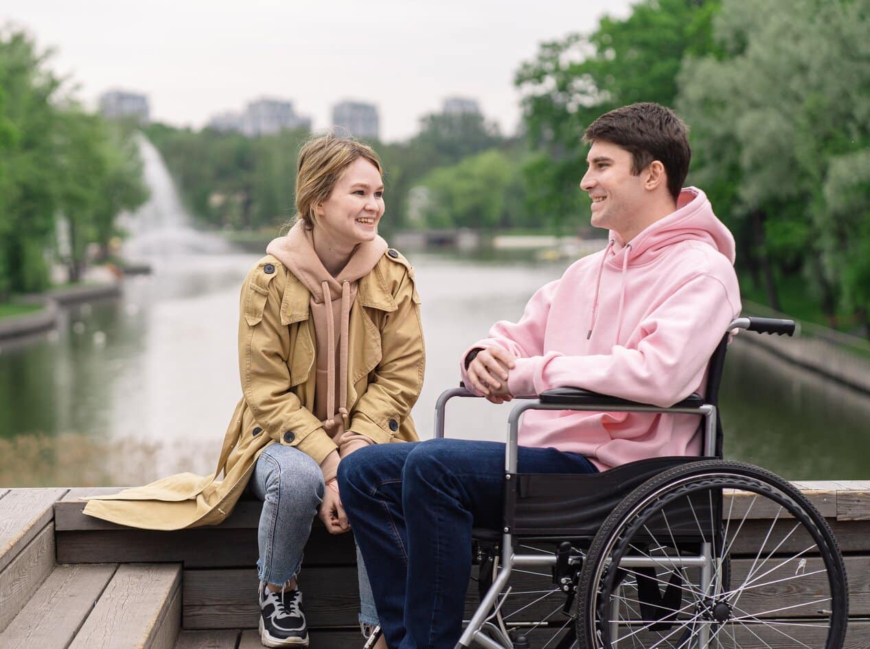 Spinal Cord Injury Counselling A man sat in his wheelchair in a park. He is sat with his partner and they are talking about spinal cord injury counselling