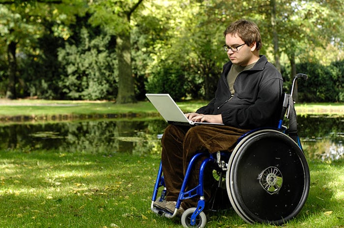 A man sat in his wheelchair with a laptop in front of him. He has had a accident which has resulted to him having spinal cord injury counselling