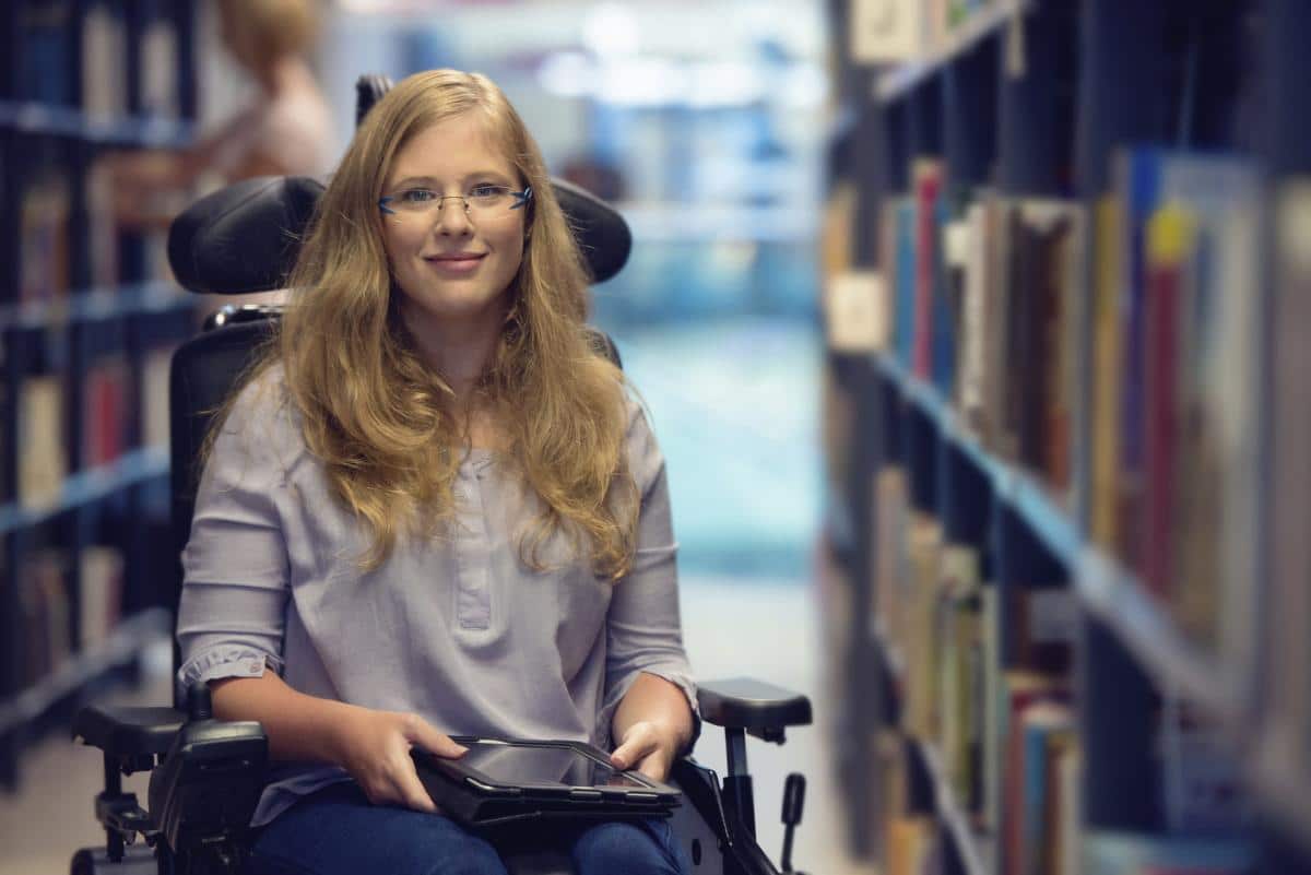 Lady with a red jacket, she is in a wheelchair looking forwards with a warm smile. She has her laptop, she is about to start a disability counselling session.